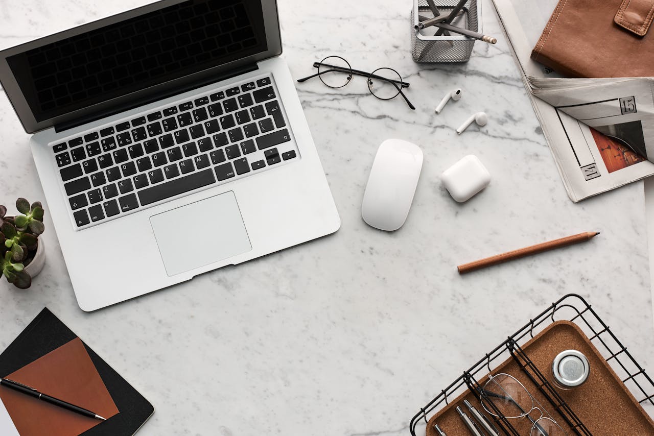 Discover a clean, organized workspace featuring a laptop, AirPods, and stationery essentials on a marble desk.